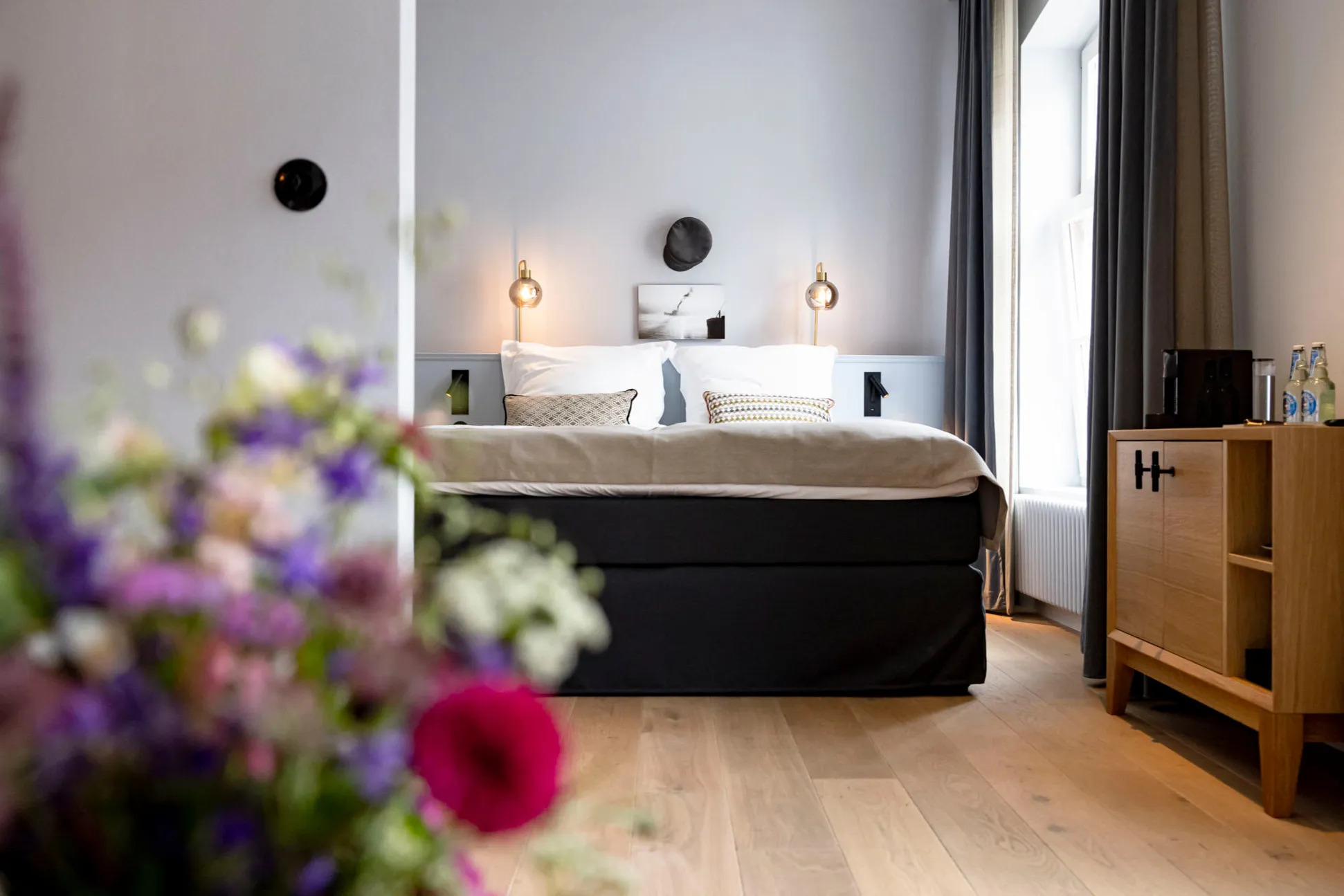 Zimmer im Boutiquehotel Petuh, im Vordergrund ein Strauß bunter Sommerblumen, dahinter das gemachte Bett am Fenster